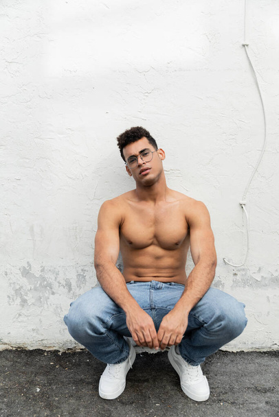 Lunghezza intera dell'uomo cubano senza camicia con corpo atletico in occhiali alla moda e jeans blu  - Foto, immagini