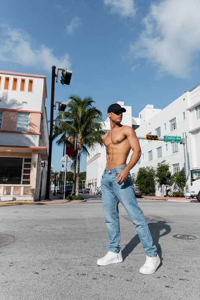 kubai férfi sportos testtel baseball sapkában és kék farmerban Miami utcáin, déli parton - Fotó, kép