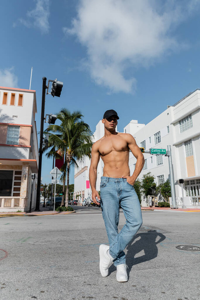 young cuban man with athletic body in baseball cap and blue jeans on street in Miami, south beach - Photo, Image
