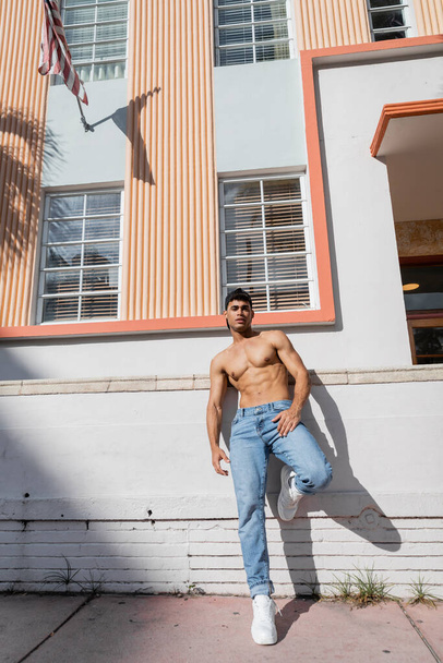 Sexy cuban man with athletic body in baseball cap and jeans standing on street in Miami - Photo, Image