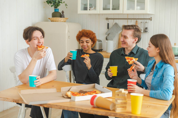 Domowe przyjęcie. Zróżnicowani przyjaciele jedzący zamówioną pizzę na domową imprezę. Happy grupa mieszane wyścigu młodych kumpli korzystających spędzając wolny weekend razem o zabawy śmiech żarty komunikowanie - Zdjęcie, obraz