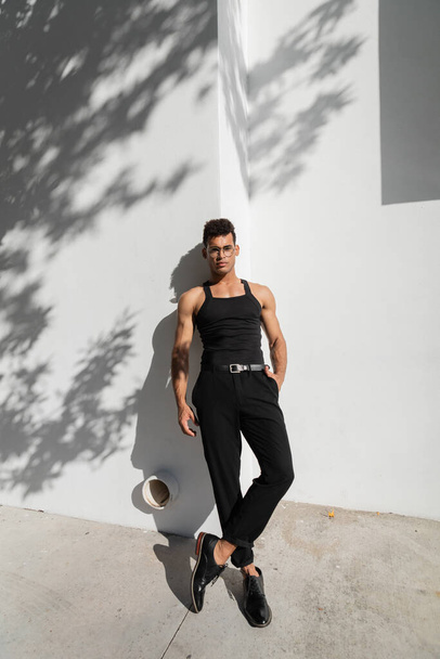 Giovane uomo cubano alla moda in posa vicino al muro bianco con ombra sulla strada urbana a Miami, spiaggia sud - Foto, immagini