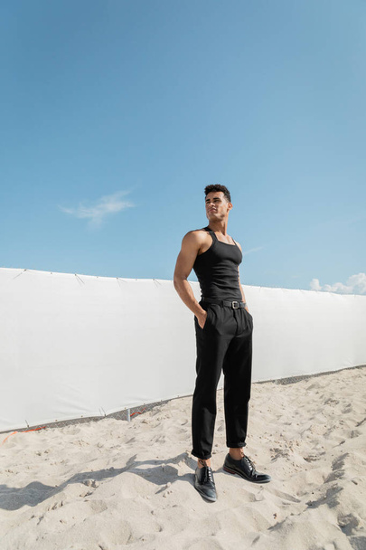 athletic young cuban man in black sleeveless t-shirt and pants posing in Miami, south beach - Photo, Image