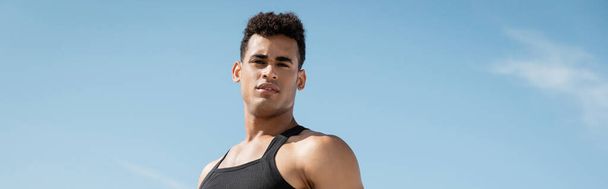 muscular young cuban man in black attire posing with sky on backdrop, banner - Photo, Image
