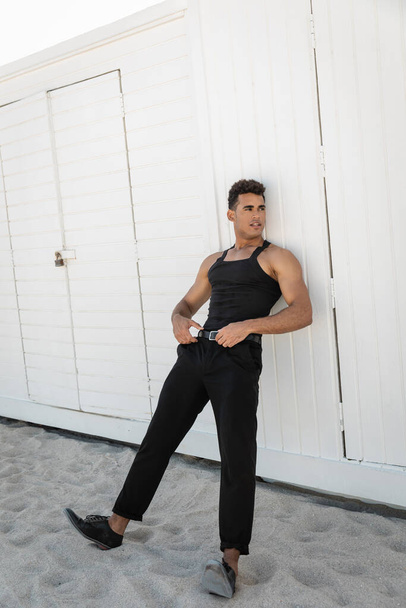Homem cubano elegante e musculoso em roupa preta tocando cinto de cintura em Miami, praia sul - Foto, Imagem