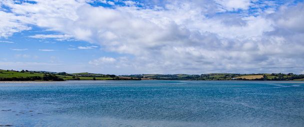 An einem Sommertag sind viele weiße Kumuluswolken am Himmel über der Meeresküste zu sehen. Irische Küstenlandschaft. Blaues Meer unter blauem Himmel und weißen Wolken - Foto, Bild