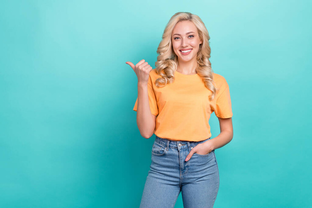 Portrait of adorable positive girl with wavy hairstyle wear yellow t-shirt indicating empty space promo isolated on teal color background. - Foto, Imagen