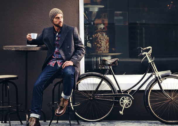Thinking, cafe and man with a coffee, bicycle and relax with thoughts, wonder and eco friendly transport. Male person, biker and guy with tea, outdoor and travel with winter fashion and a cappuccino. - Fotó, kép