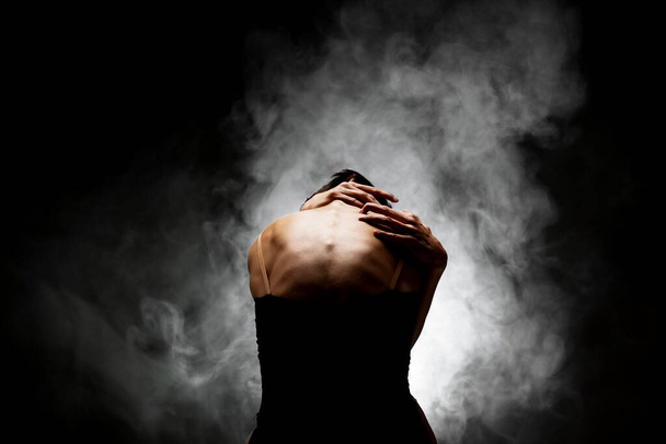 half silhouette modern ballet dancer posing on dark background with smoke - Foto, afbeelding