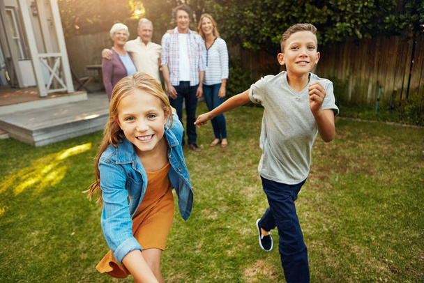 Я швидший за тебе. молодий брат і сестра грають у дворі зі своєю сім'єю на задньому плані
 - Фото, зображення