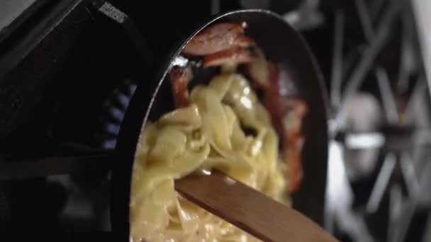 close-up μιας ξύλινης σπάτουλας ανακατέψτε ζυμαρικά με κοτόπουλο σε ένα τηγάνι. Η έννοια της μαγειρικής. κατακόρυφο βίντεο. - Πλάνα, βίντεο