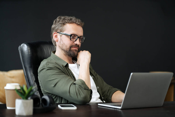 Wise, caucasian man captured in portrait, sitting at desk in home office. He appearing thoughtful, as he works on computer. Sense of professionalism and productivity in a home work environment. High - 写真・画像