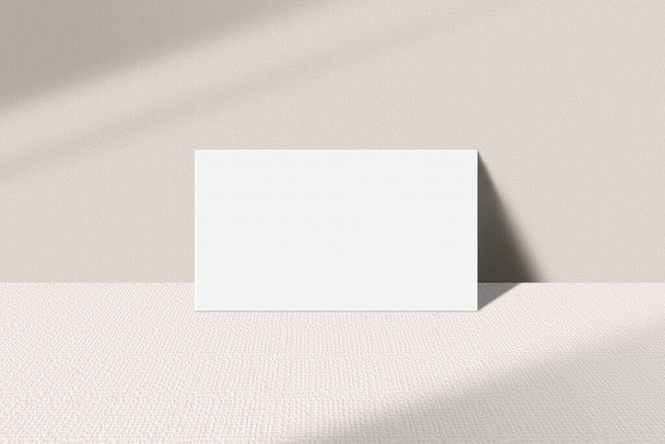 Realistic business card mockup leaning on the table. Simple blank business card on an elegant light background. Business card mock up with shadow overlay effect - 写真・画像