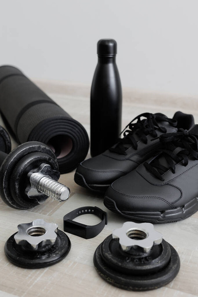 Concepto deportivo - mancuernas, esterilla deportiva, zapatos, reloj y botella de agua en el suelo de madera - Foto, imagen