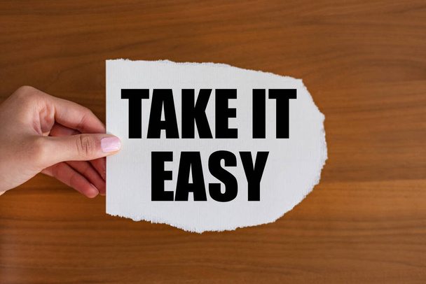 Take it easy. Woman hand holds a piece of paper with a note, take it easy. Motto, positive emotion, never mind, relaxation, and cool attitude, wellbeing. - Photo, image