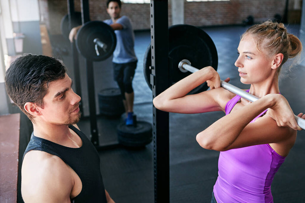 Set a goal and make it happen. a young woman lifting weights with her personal trainer assisting her - Foto, Bild