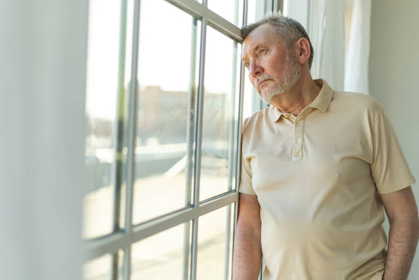 Λυπημένος κουρασμένος μοναχικός απογοητευμένος ηλικιωμένος άνδρας στο σπίτι μόνος. Δυστυχισμένος παππούς κοιτάζοντας δυστυχώς έξω από το παράθυρο βιώνει θλίψη σχετικά με το θάνατο άσχημα νέα. Στρεσαρισμένος ηλικιωμένος που υποφέρει από μοναξιά - Φωτογραφία, εικόνα