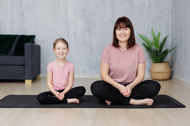 Familien- und Sportkonzept - junge Mutter mit kleiner Tochter praktiziert Yoga zu Hause - Foto, Bild