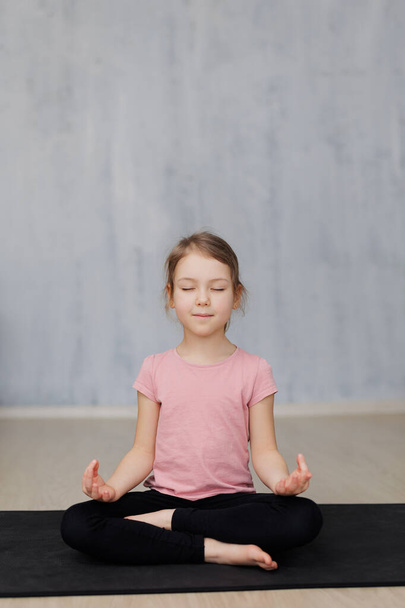 cute little girl doing yoga exercises on yoga mat at home, copy space over grey wall background - Foto, imagen