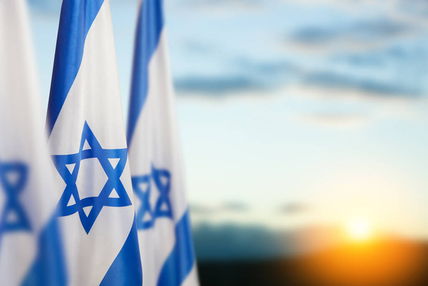 Israel flags with a star of David over cloudy sky background on sunset. Patriotic concept about Israel with national state symbols. Banner with place for text. - Φωτογραφία, εικόνα