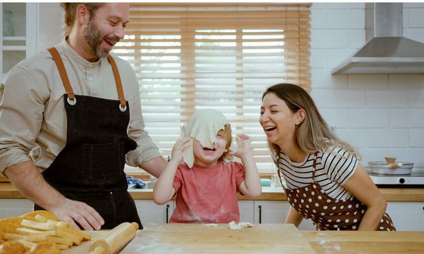 Father and mother teaching baby son kneading dough on kitchen counter at home. Parents and boy kid enjoy and fun indoors activity cooking together. - Photo, Image