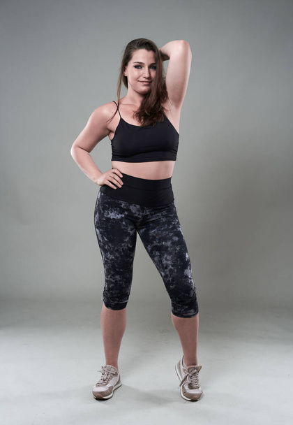 Attractive plus size woman in fitness top and tights, gray background - Fotografie, Obrázek