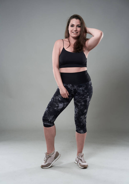 Attractive plus size woman in fitness top and tights, gray background - Foto, Bild