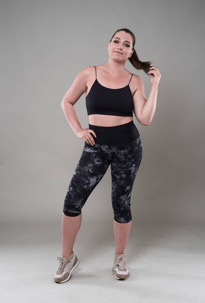 Attractive plus size woman in fitness top and tights, gray background - Valokuva, kuva