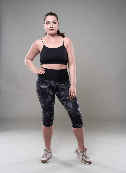 Attractive plus size woman in fitness top and tights, gray background - Fotó, kép