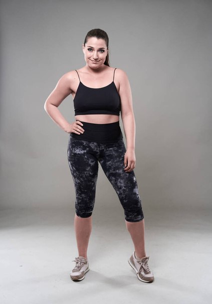 Attractive plus size woman in fitness top and tights, gray background - 写真・画像