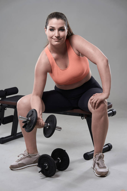 Strong confident plus size young woman working out fitness exercises with dumbbells - 写真・画像