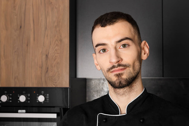 Portrét kuchaře v černé uniformě v kuchyni - Fotografie, Obrázek