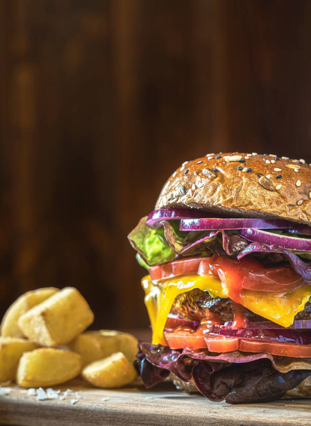 Close-up of a delicious burger with vegetables and fries on a dark wooden table. Lettuce, tomato, onion and cheese. Warm atmosphere. Wooden background - Φωτογραφία, εικόνα