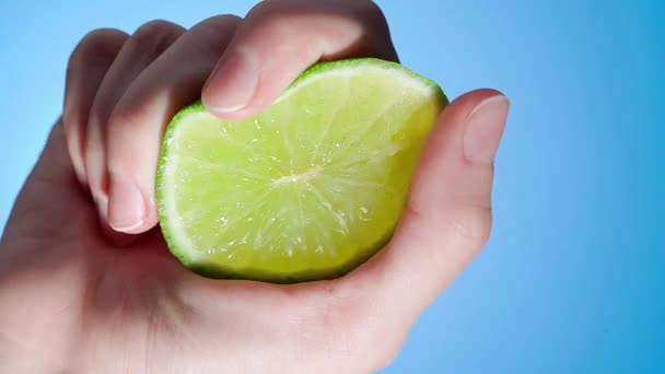 Hand squeezes lime slice and juice flows out on blue background - Footage, Video