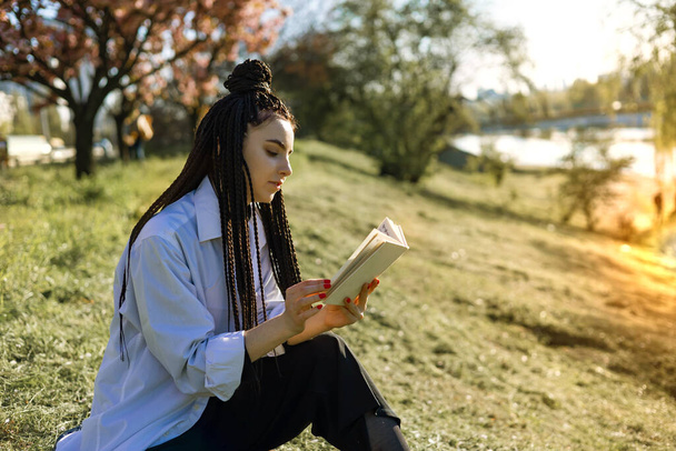 Junge Frau mit Dreadlocks liest Buch im Frühlingspark. - Foto, Bild