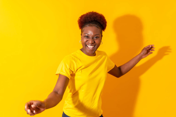 Sarı bir arka planda izole edilmiş genç Afrikalı Amerikalı kadın gülümsüyor ve dans ediyor. - Fotoğraf, Görsel