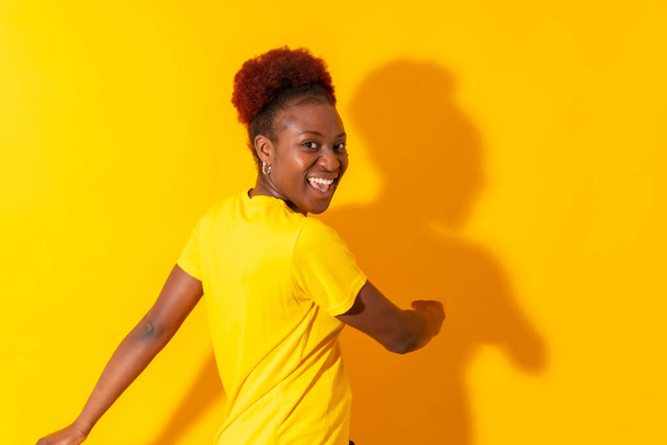 Young african american woman isolated on a yellow background smiling and dancing, studio shoot - Foto, immagini
