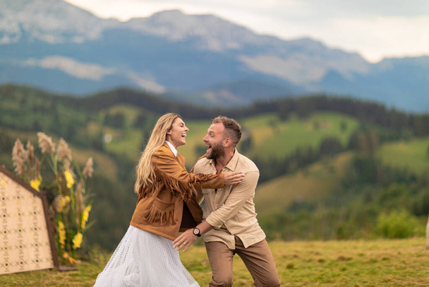 paar loopt, lacht, bruid springt op bruidegom 's rug, met diepe liefde, met bergen op de achtergrond. - Foto, afbeelding