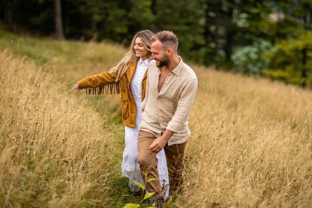 Una pareja feliz paseando por una hierba alta en un sendero, con él guiándola de la mano y ella riendo con alegría y amor. - Foto, imagen