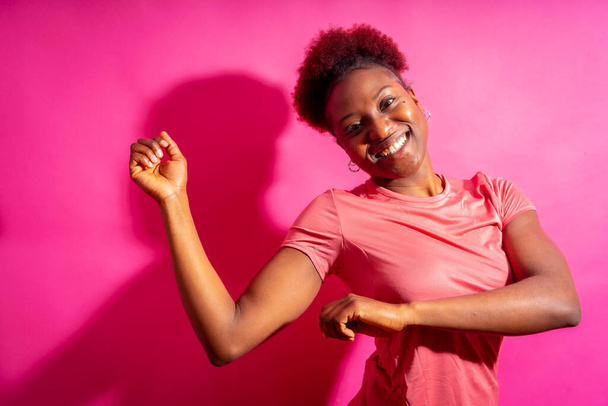 Young african american woman isolated on a pink background smiling and dancing, studio shoot - Valokuva, kuva