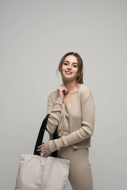 Brunette cheerful millennial woman holding white eco bag standing over white studio background. Concept of recycle for better environment. No plastic. Fashion and ecology concept - Foto, imagen