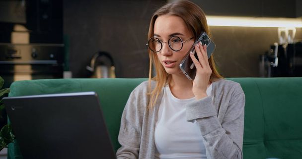 Smiling young business woman professional talking on phone using laptop sit at home. Lady holding mobile phone call conversation with client, giving professional consultation or advice, making sales. - Фото, изображение