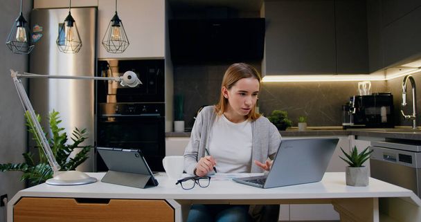 Junge Unternehmerin mit Laptop Schreibnotizen in modernen Schreibtisch zu Hause. Online von zu Hause aus Webkurs oder Höranleitung ansehen. Fernstudienkonzept. - Foto, Bild