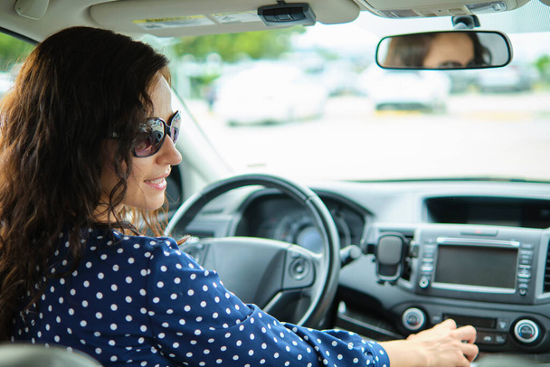 Νεαρή κομψή γυναίκα οδηγός κάθεται πίσω από το τιμόνι του αυτοκινήτου της. Έννοια του οχήματος οδήγησης. - Φωτογραφία, εικόνα