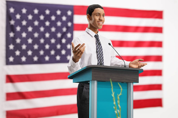 Happy young african american man on a pedestal giving a speech in front of a USA flag - Foto, Bild