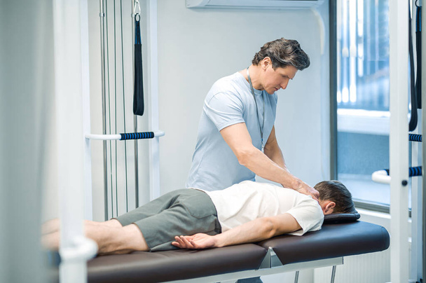 Back rehabilitation. Manual therapist working with patient back and looking involved - 写真・画像