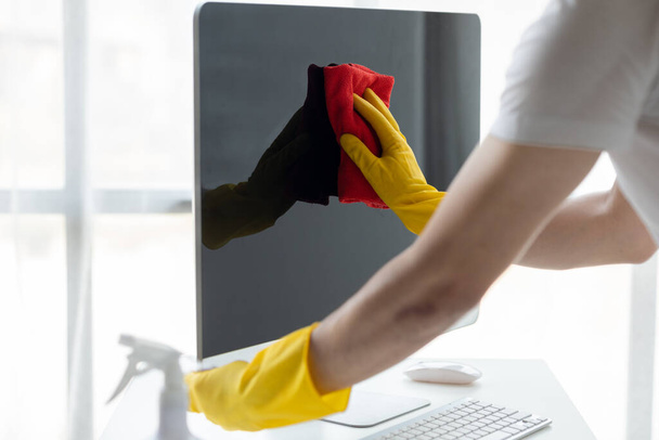 Schoonmaakruimte, schoonmaakmedewerker gebruikt doek om computerscherm af te vegen in bedrijfsruimte. Schoonmaakpersoneel. Concept van reinheid in de organisatie. - Foto, afbeelding