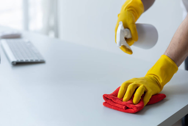 La personne qui nettoie la pièce, le personnel de nettoyage utilise un chiffon et pulvérise du désinfectant pour essuyer la table dans la salle de bureau de l'entreprise. Personnel de nettoyage. Maintenir la propreté de l'organisation. - Photo, image