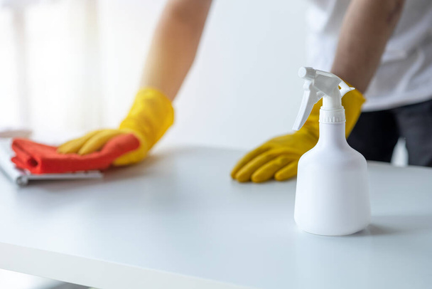 Osoba sprzątająca pokój, personel sprzątający używa tkaniny i środka dezynfekującego do wycierania stołu w biurze firmy. Sprzątacze. Utrzymanie czystości w organizacji. - Zdjęcie, obraz