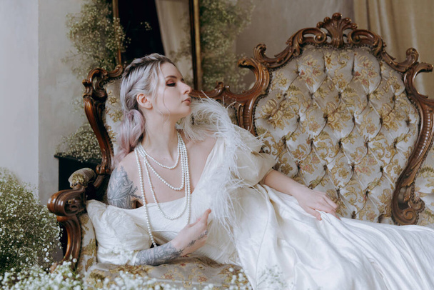 A luxurious girl with a beautiful make-up and hairstyle in a vintage vintage dress woke up in the morning in bed and sits on the sofa at the piano and poses as a model - Zdjęcie, obraz